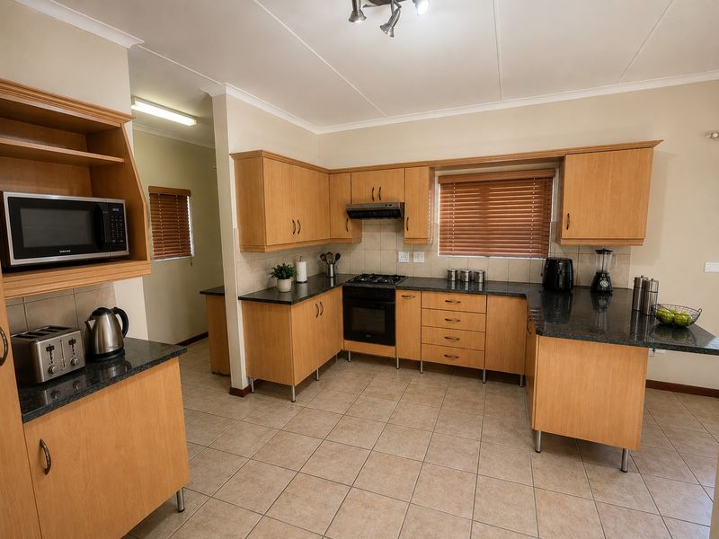 A functional kitchen featuring light wood cabinetry, granite countertops, a gas hob, built-in oven, and tiled flooring with a pass-through to a secondary area.