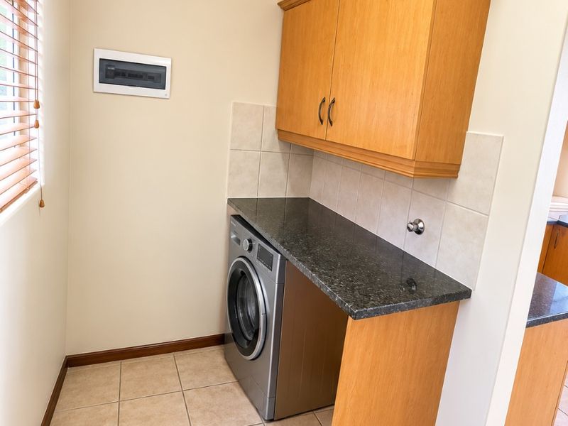 A functional laundry area featuring built-in wooden cabinetry, granite countertops, tiled splashbacks, and tiled flooring with an integrated electrical distribution board.