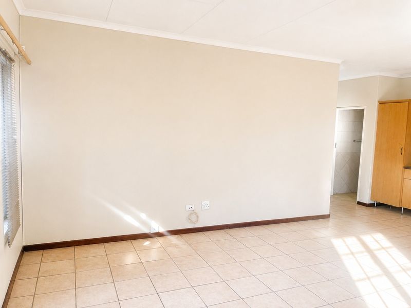 A bright, empty living area featuring neutral tiled flooring, a built-in cupboard, and natural light from the window.