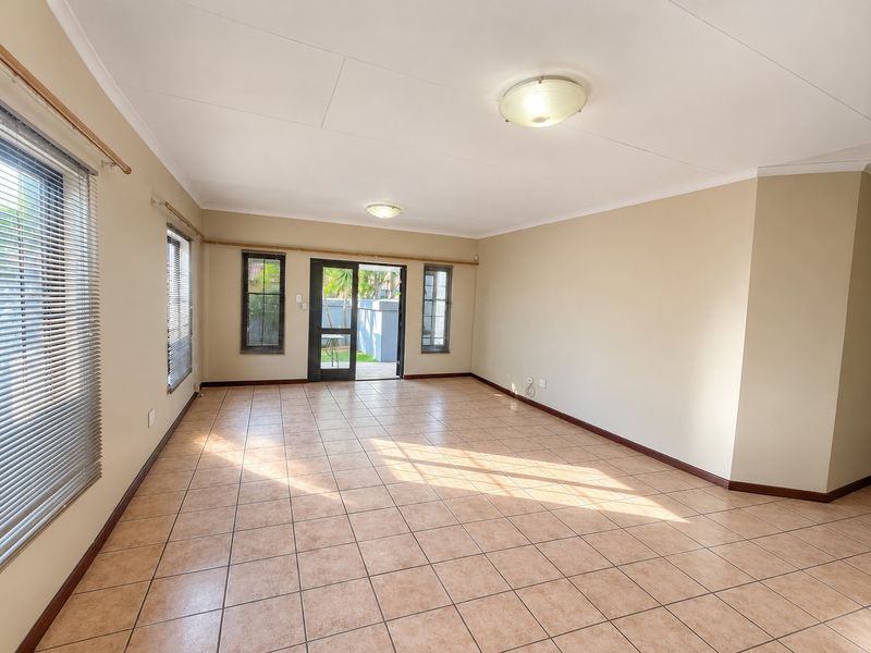 A spacious, empty living room featuring neutral tiled flooring, flush mount lighting, and direct access to an outdoor area through a glass door.