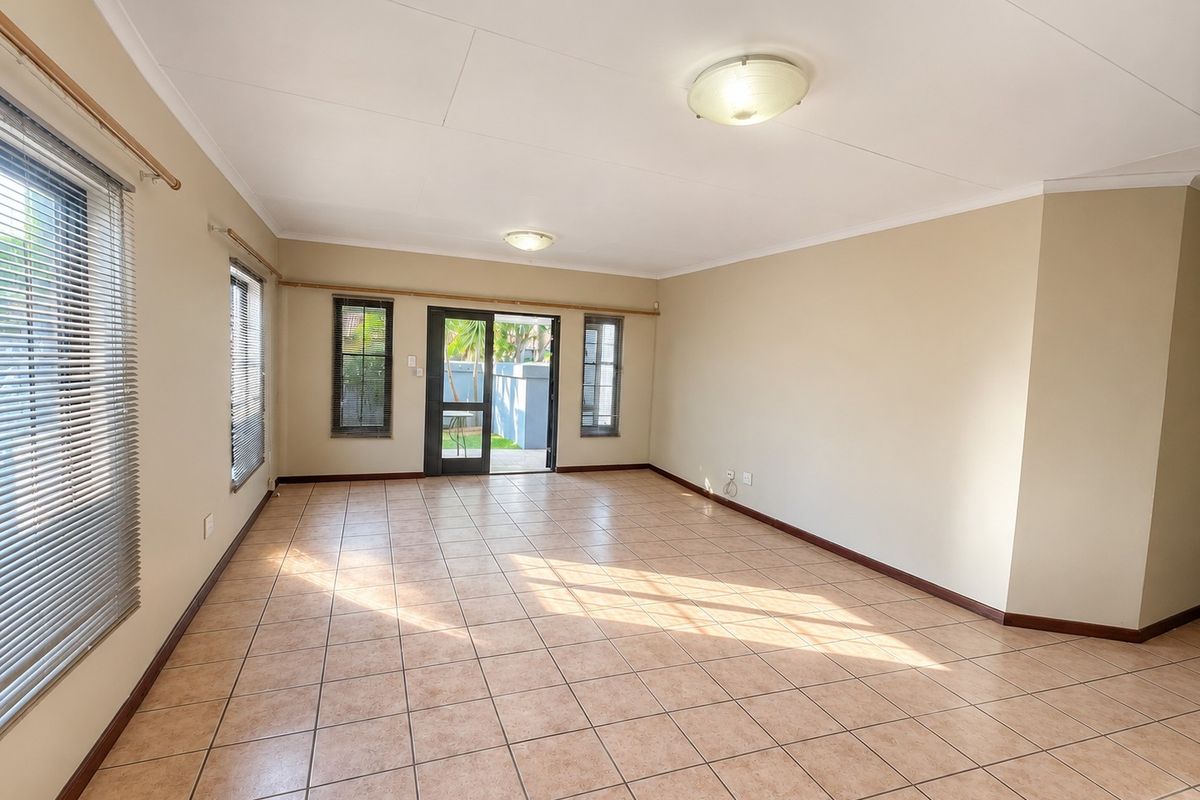 A spacious, empty living room featuring neutral tiled flooring, flush mount lighting, and direct access to an outdoor area through a glass door.
