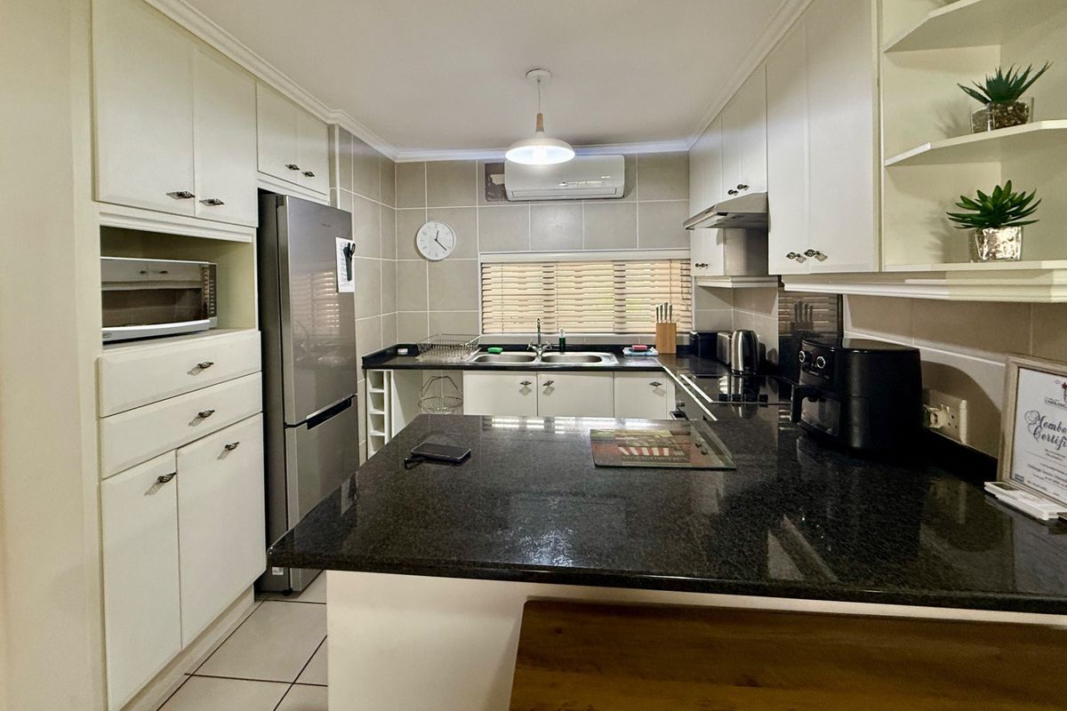 A well-maintained kitchen featuring white cabinetry, dark granite countertops, a double basin sink, and a tiled backsplash with an integrated air conditioning unit.