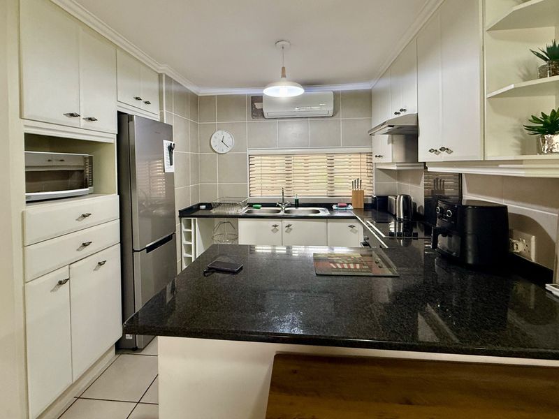 A well-maintained kitchen featuring white cabinetry, dark granite countertops, a double basin sink, and a tiled backsplash with an integrated air conditioning unit.