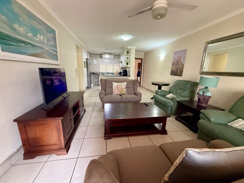 Open-plan living area featuring tiled flooring, a ceiling fan, and a functional kitchen space with built-in cabinetry and countertops.