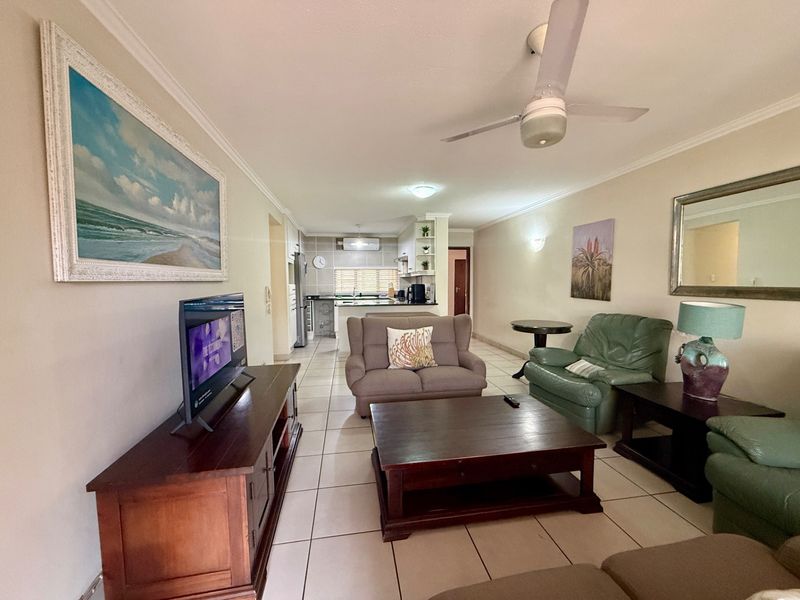 Open-plan living area featuring tiled flooring, a ceiling fan, and a connected kitchen space with built-in cabinetry and countertops.