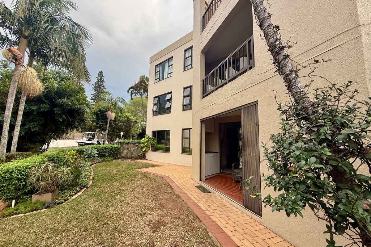 Rear view of the apartment building featuring a ground floor patio, upper-level balconies, paved garden pathways, and established landscaping.