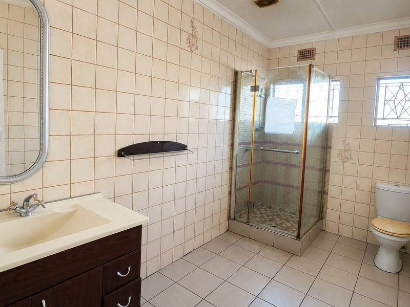 A functional bathroom featuring a vanity cabinet, a separate shower enclosure, and a toilet, finished with neutral wall and floor tiling.