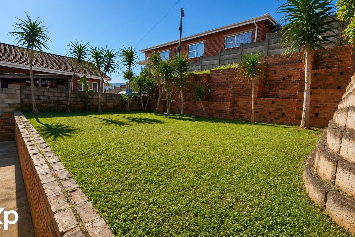 A spacious rear garden featuring tiered brick retaining walls, a well-maintained lawn, and concrete boundary walls providing privacy.