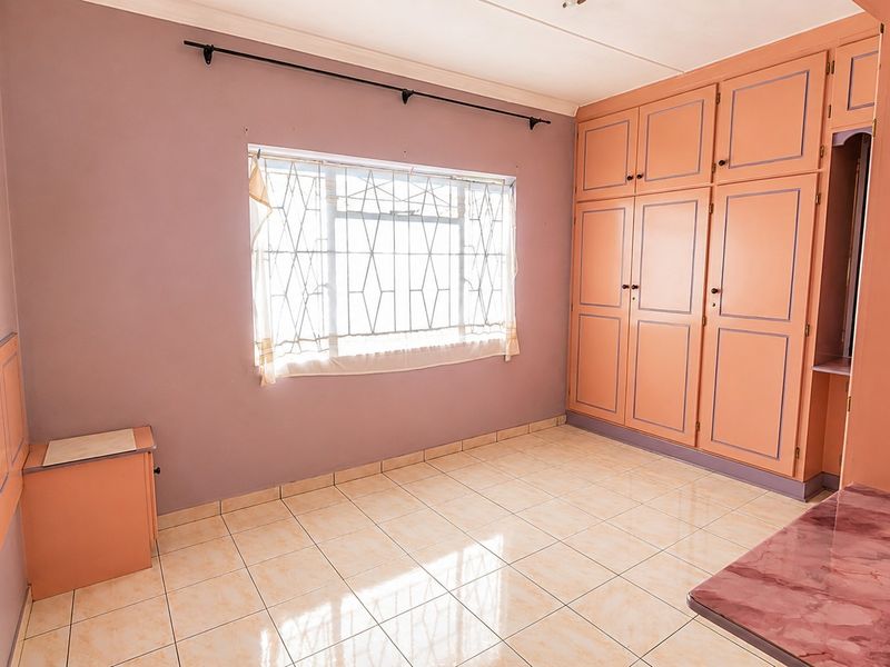 A vacant bedroom featuring tiled flooring, built-in cupboards, and a window with security bars, offering a blank canvas for renovation.