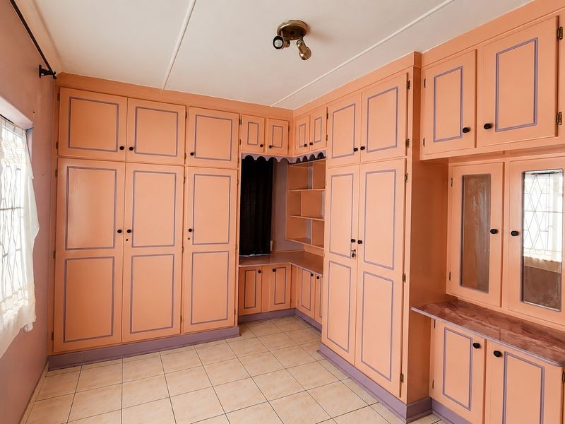 A spacious bedroom featuring extensive built-in cabinetry with a vanity area and tiled flooring, offering significant storage potential.