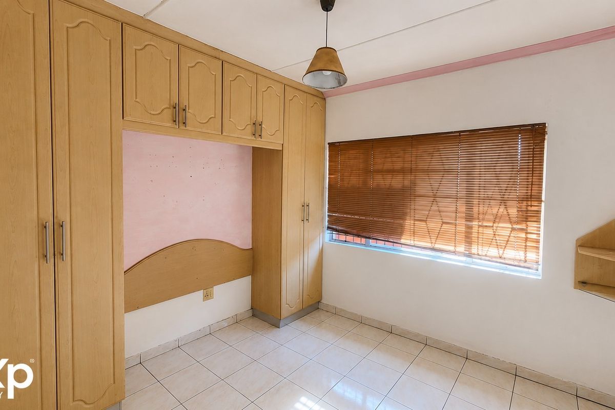 A bedroom featuring built-in wooden cupboards with an integrated headboard, tiled flooring, and venetian blinds.