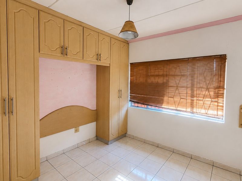 A bedroom featuring built-in wooden cupboards with an integrated headboard, tiled flooring, and venetian blinds.