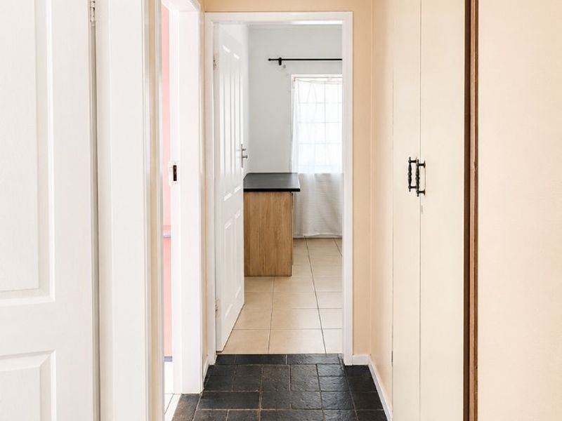 A bright hallway featuring dark tiled flooring, built-in storage cupboards, and coved cornicing, leading through to an adjacent room.