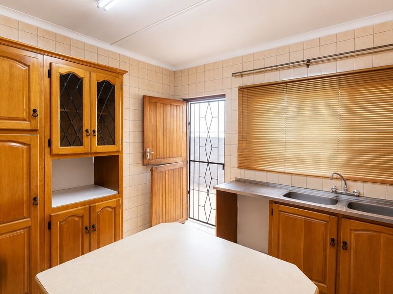 A functional kitchen featuring classic wooden cabinetry, tiled walls, a double stainless steel sink, and a stable door leading to the exterior.