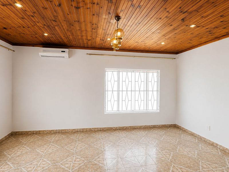A bright, empty living area featuring a warm timber ceiling, ceramic tiled flooring, and a wall-mounted air conditioning unit.