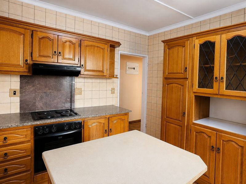 A traditional kitchen featuring wooden cabinetry, stone countertops, a built-in oven with hob, and tiled splashbacks, offering a functional and classic layout.