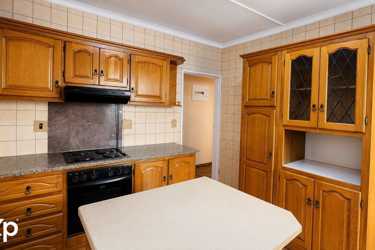 A traditional kitchen featuring wooden cabinetry, stone countertops, a built-in oven with hob, and tiled splashbacks, offering a functional and classic layout.