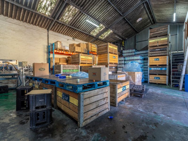 Industrial utility space featuring high ceilings with corrugated metal roofing, skylights, exposed brick walls, and durable concrete flooring suitable for storage or production.