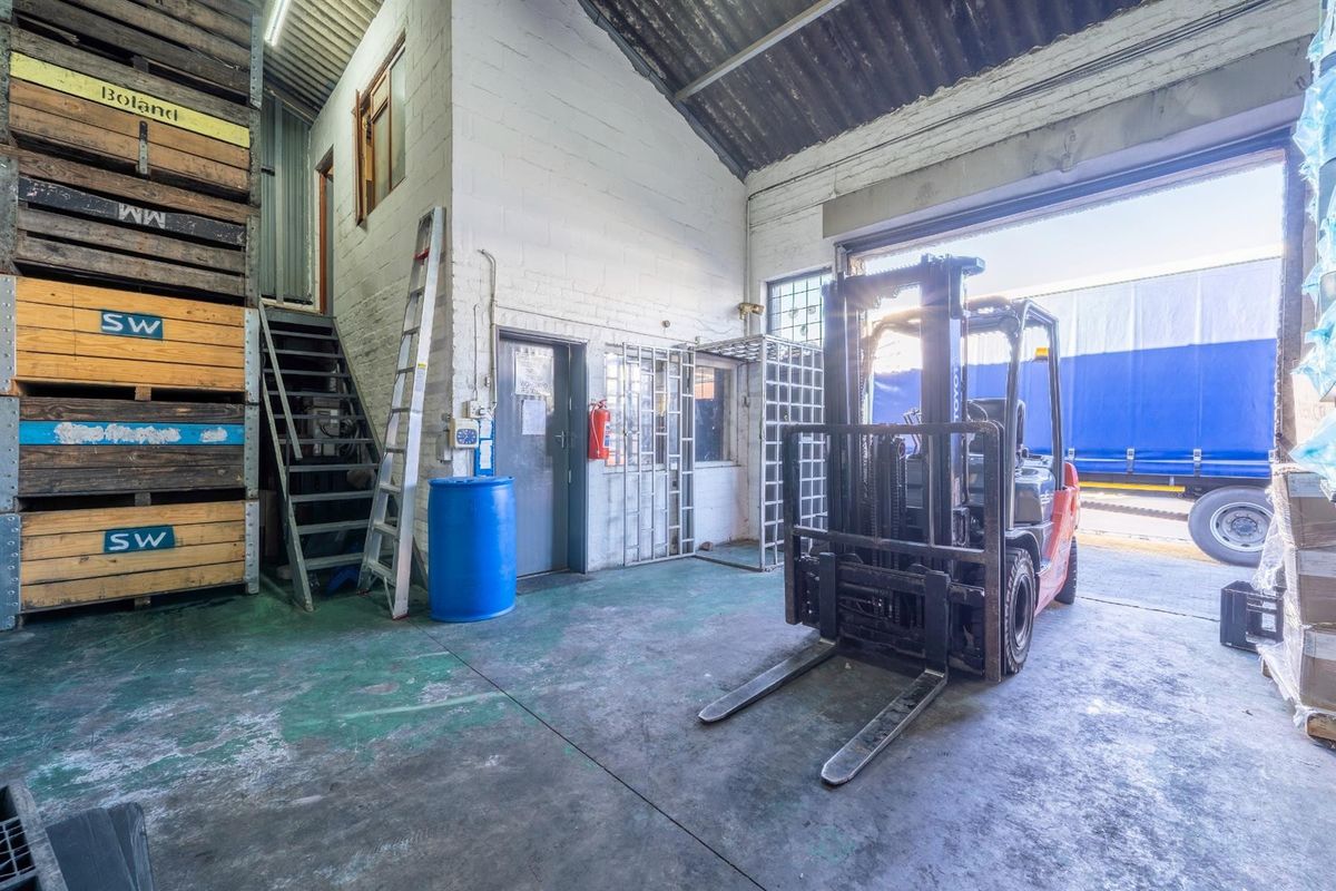 Industrial warehouse space featuring high ceilings, concrete flooring, a metal staircase, and a large roller shutter door for vehicle access.