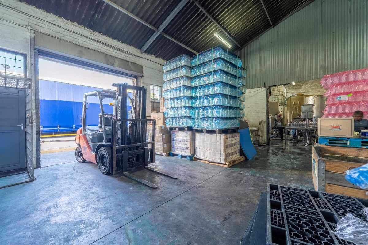 Industrial warehouse space featuring high ceilings with exposed steel trusses, concrete flooring, and a large roller shutter door for efficient loading access.