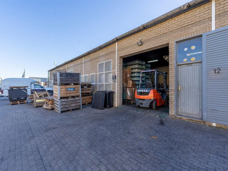 Industrial unit exterior featuring a brick facade, paved driveway, and a large roller door entrance, suitable for warehouse or light industrial operations.