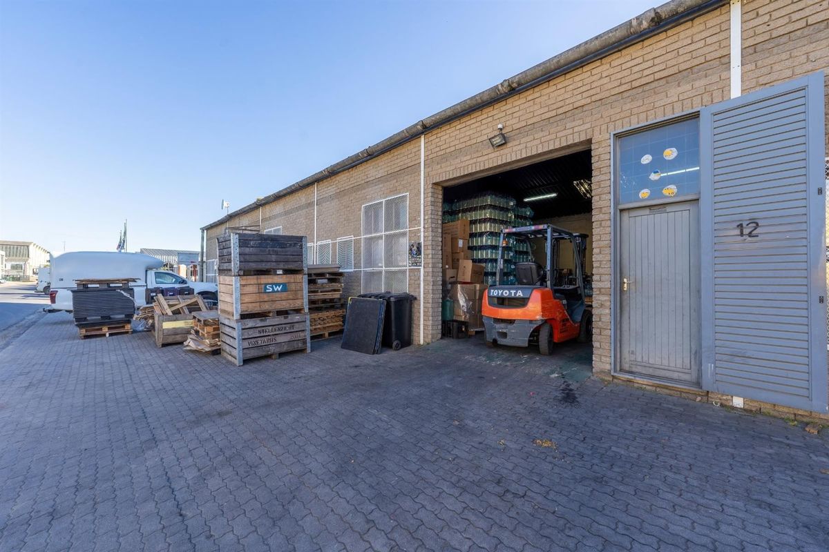 Industrial unit exterior featuring a brick facade, paved driveway, and a large roller door entrance, suitable for warehouse or light industrial operations.