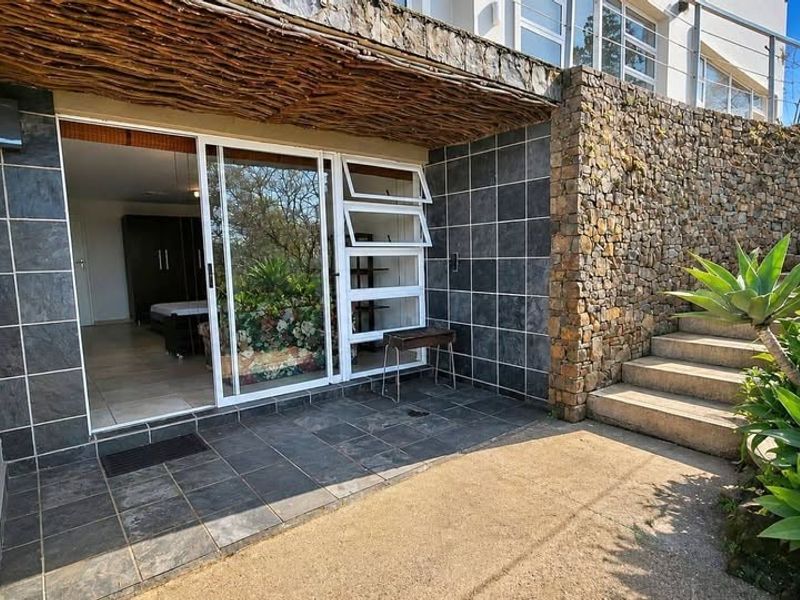 A covered patio area featuring slate tiling, stone wall cladding, and a rustic thatched roof overhang, providing direct access to the interior living space.