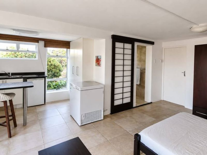 Open-plan living space featuring a kitchenette with a breakfast bar, tiled flooring, and direct access to an adjoining bathroom area.