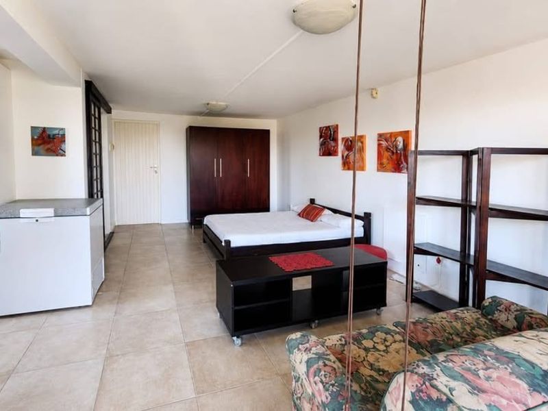 An open-plan living and sleeping area featuring neutral tiled flooring and built-in storage cabinetry.