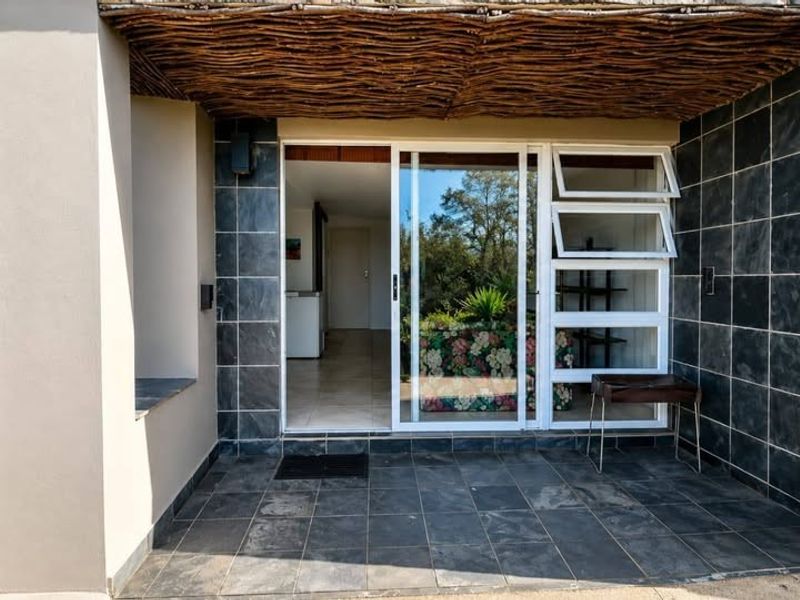 A covered patio area featuring slate tile flooring, natural stone wall accents, and a rustic thatched ceiling, providing a seamless transition to the interior.
