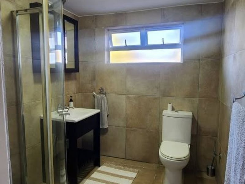 A functional bathroom featuring a corner shower enclosure, vanity unit with basin, toilet, and neutral floor-to-ceiling tiling.