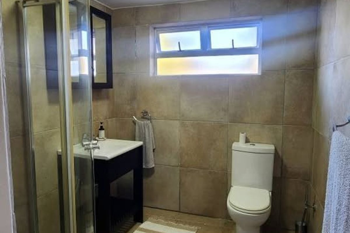 A functional bathroom featuring a corner shower enclosure, vanity unit with basin, toilet, and neutral floor-to-ceiling tiling.