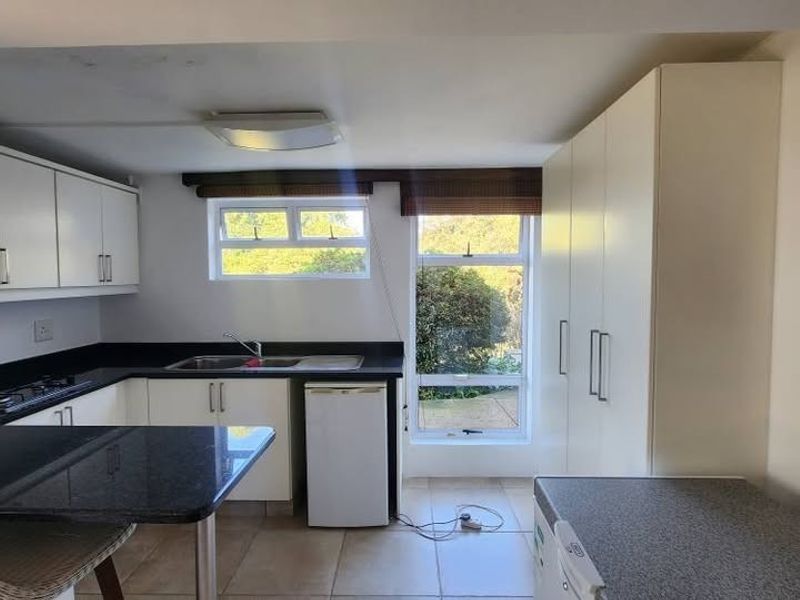 A functional kitchen featuring white cabinetry, dark granite countertops, a gas hob, and tiled flooring with ample storage space.