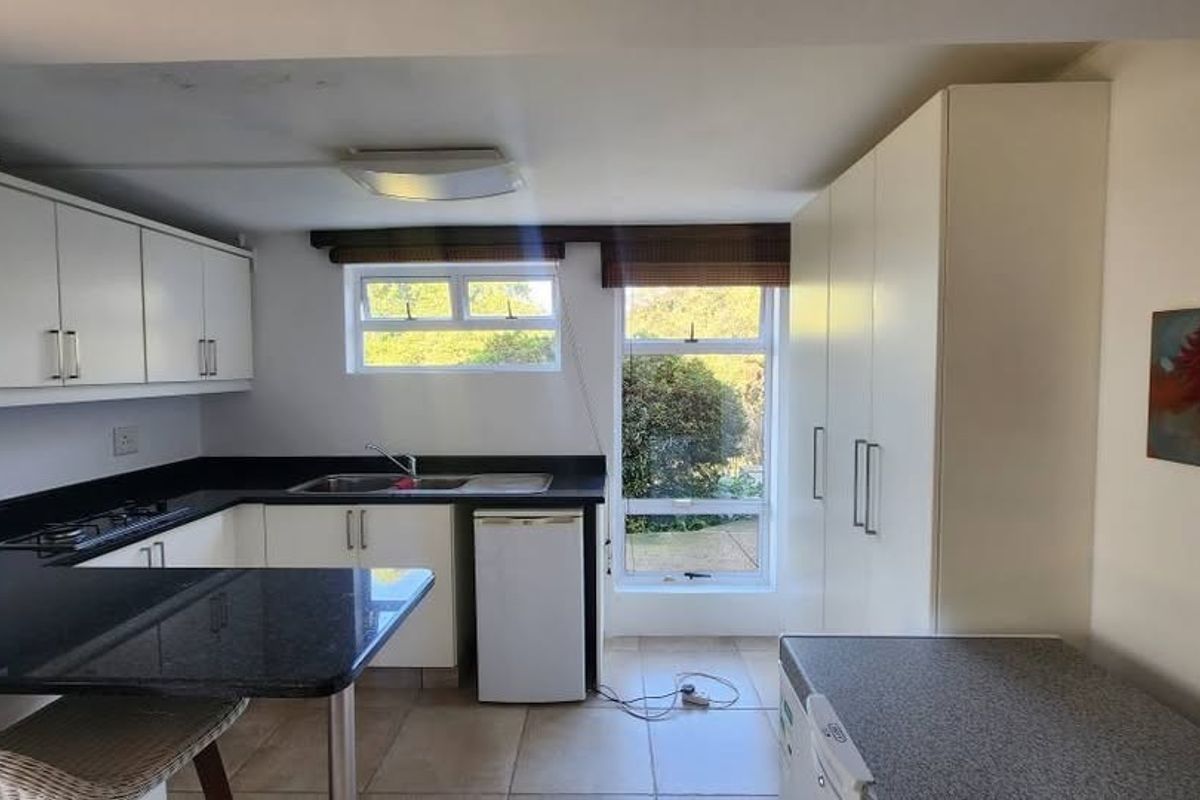 A functional kitchen featuring white cabinetry, dark granite countertops, a gas hob, and tiled flooring with ample storage space.