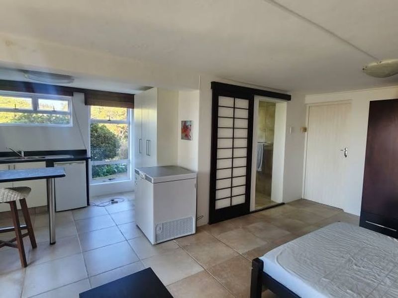 Open-plan studio space featuring a kitchenette with built-in cabinetry, tiled flooring, and a built-in wardrobe, offering a functional living and sleeping area.