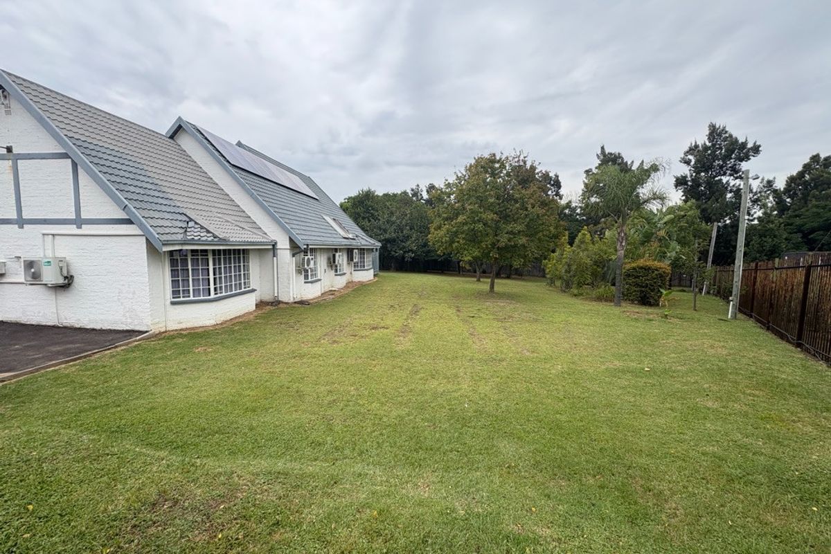 Spacious rear garden featuring a well-maintained lawn, mature trees, and the rear elevation of the residence with solar panels and bay windows.
