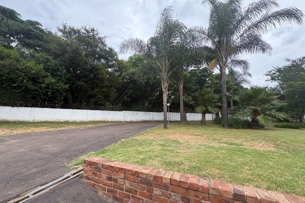 A view of the property entrance featuring an asphalt driveway, a brick retaining wall, and established palm trees along the perimeter boundary.