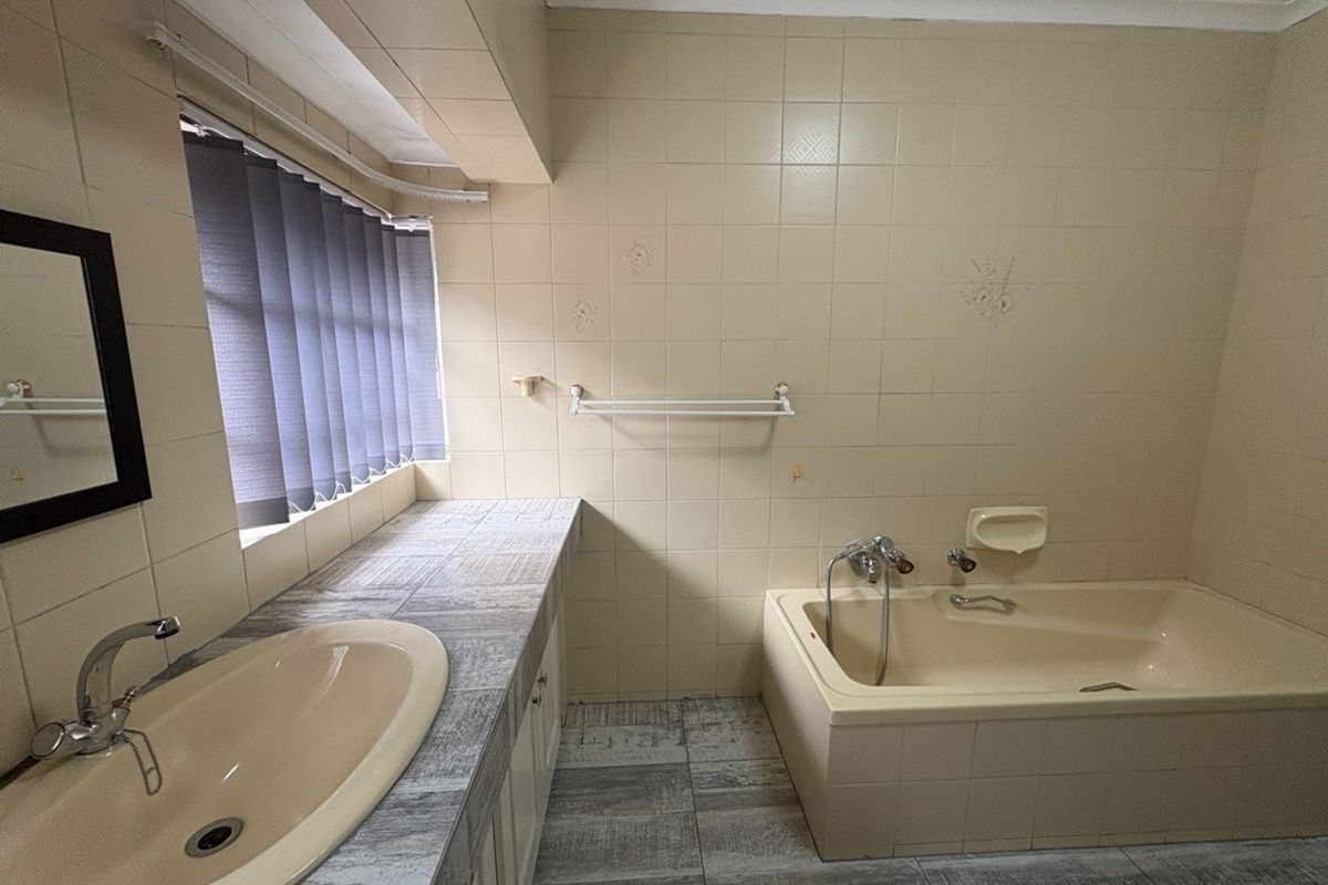 A functional bathroom featuring a built-in bathtub, vanity with drop-in basin, and neutral wall tiling, offering a clean space ready for modern updates.