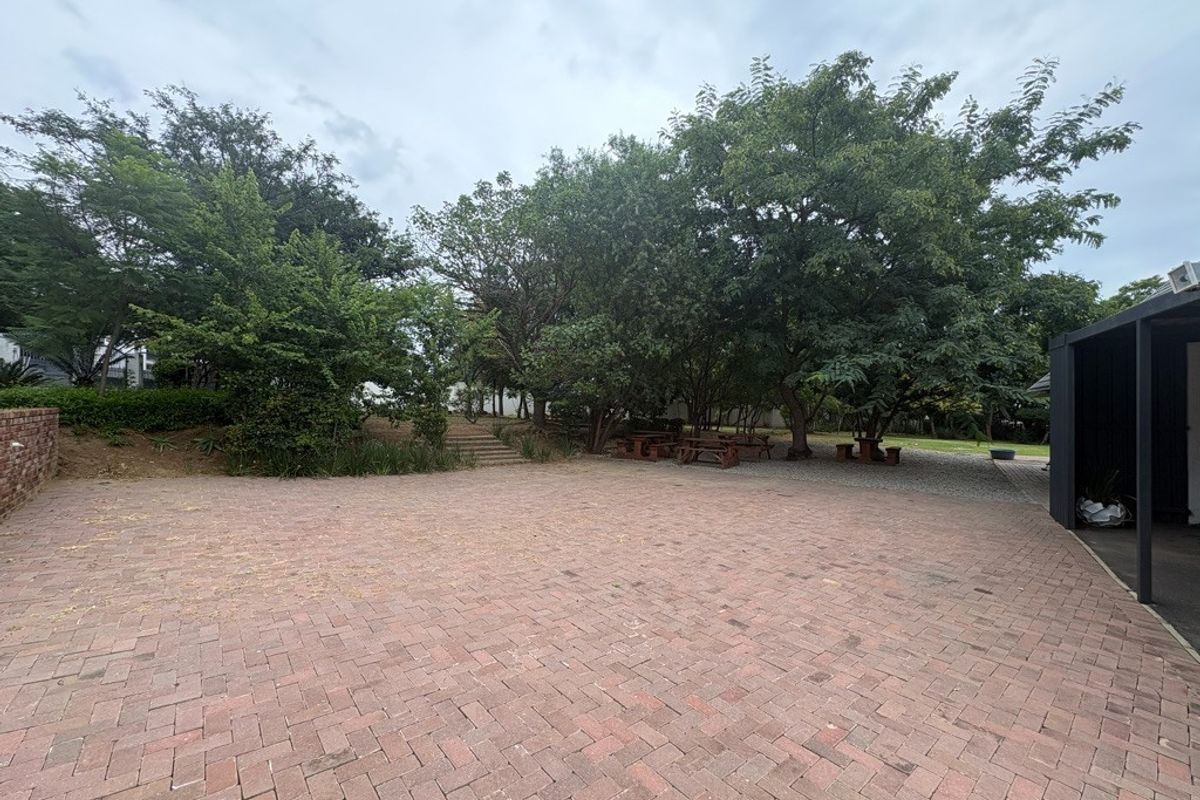 A spacious outdoor area featuring extensive brick paving, mature trees, and stone steps leading to a landscaped garden section.