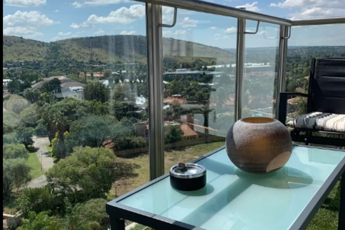 A private balcony featuring a modern glass balustrade with stainless steel railings, offering elevated views over the surrounding landscape.