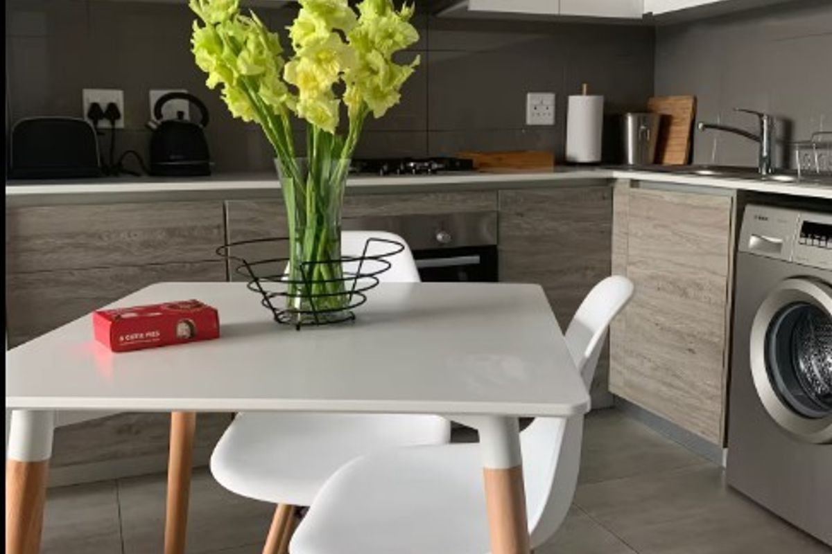 Modern kitchen featuring sleek white and wood-grain cabinetry, integrated appliances, stainless steel sink, and neutral tiled flooring.