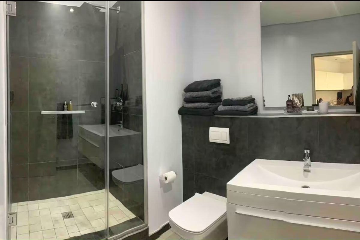 Modern bathroom featuring a glass-enclosed shower, wall-mounted vanity with basin, wall-hung toilet, and large mirror with dark grey tiled accents.