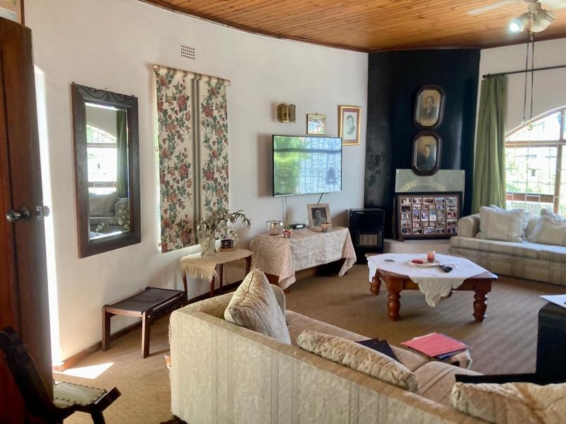 A living room featuring a timber ceiling, fireplace, and arch window, currently showing dated finishes and worn carpeting.