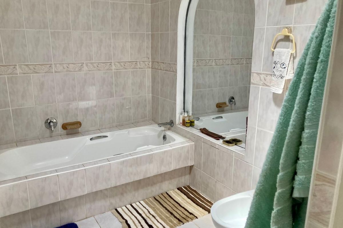 A functional bathroom featuring a built-in bathtub, tiled wall finishes, and a large arched mirror above the tub area.