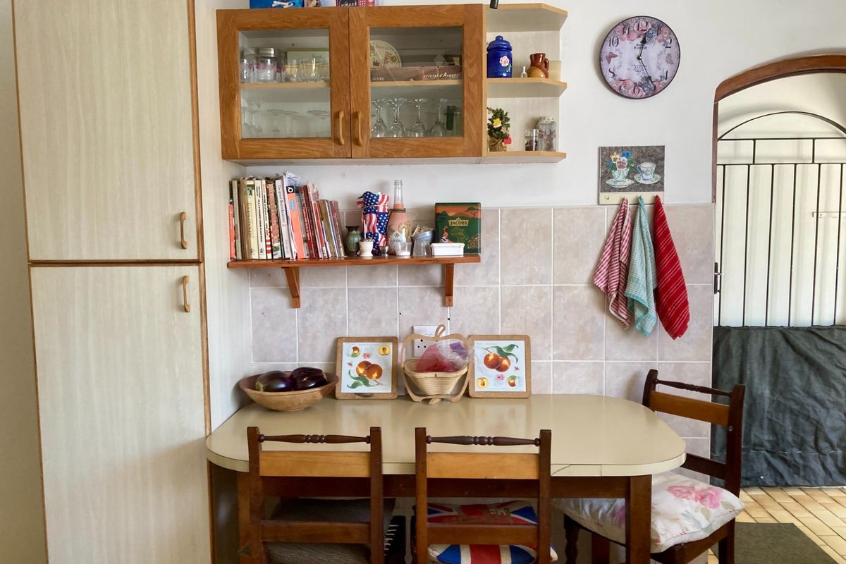 A functional kitchen corner featuring built-in cabinetry, a tiled backsplash, and a dining area, leading through an archway to an adjacent space.