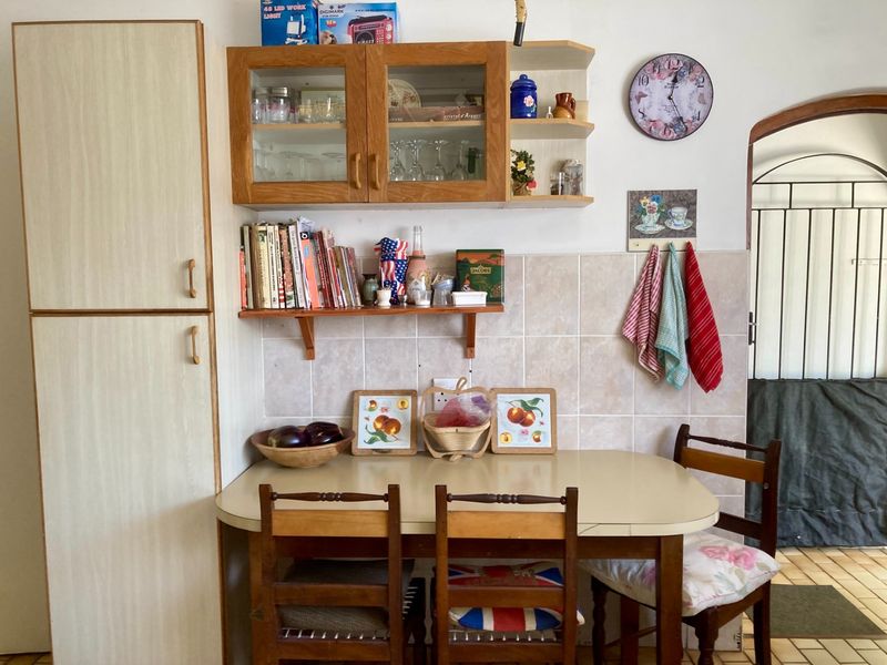 A functional kitchen corner featuring built-in cabinetry, a tiled backsplash, and a dining area, leading through an archway to an adjacent space.