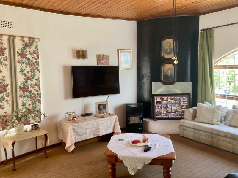 A living room featuring a timber ceiling, carpeted flooring, and a corner fireplace, offering a traditional layout with potential for modernization.