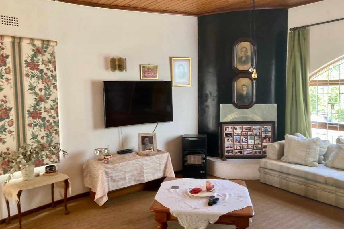 A living room featuring a timber ceiling, carpeted flooring, and a corner fireplace, offering a traditional layout with potential for modernization.