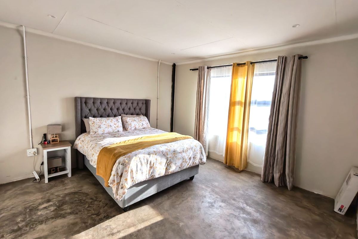 Spacious bedroom featuring polished concrete flooring, recessed lighting, and large windows with natural light, finished with exposed surface-mounted electrical conduit.