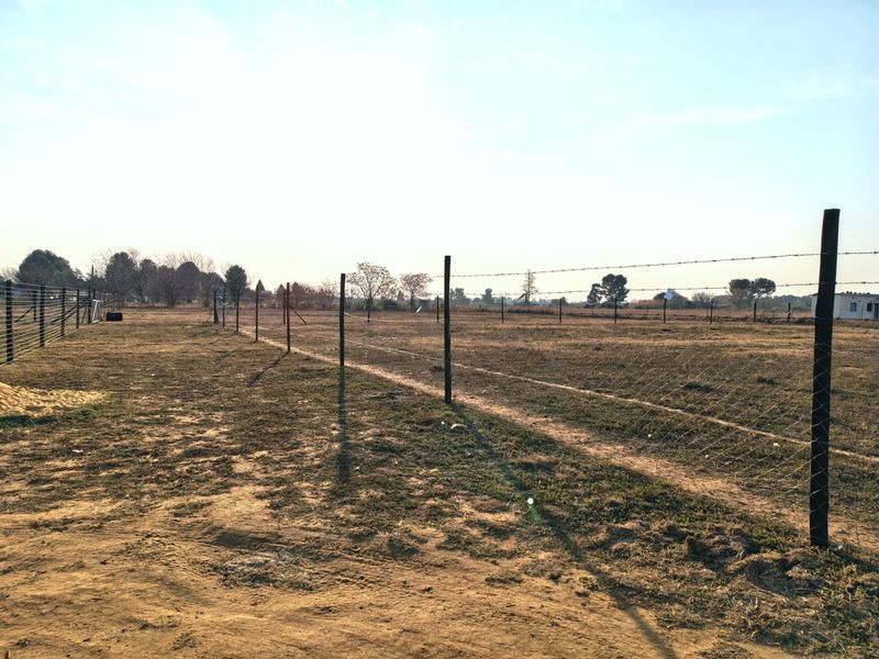 Expansive open land area featuring perimeter barbed wire fencing and wooden posts, suitable for agricultural or small holding use.